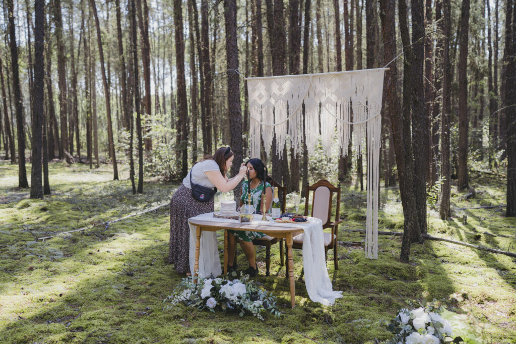 A boho bride getting her makeup done by a make-up artist in the forest during a photographer workshop. 