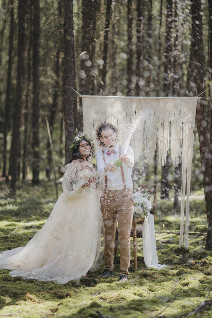 A boho bride and groom popping champagne after getting married in the forest.