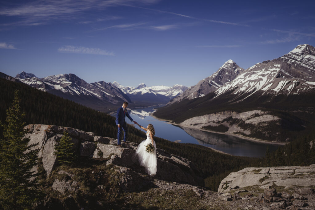 Groom helping his bride onto the mountain during a canmore elopement with their canmore photographer. 