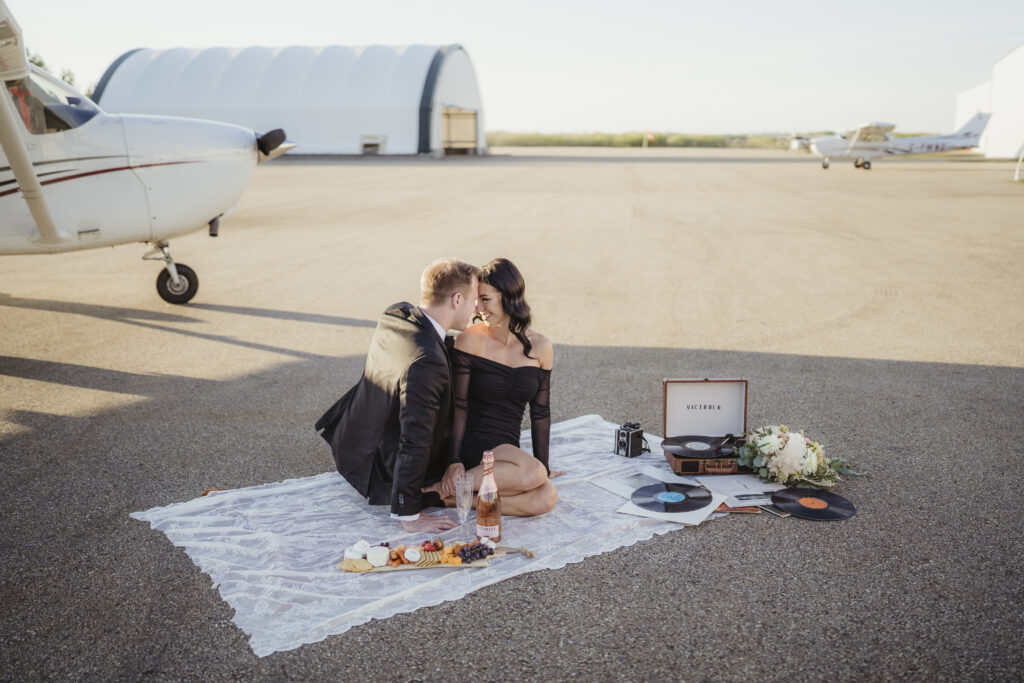 Couple enjoying an engagement picnic in front of an airplane for their engagement session. 